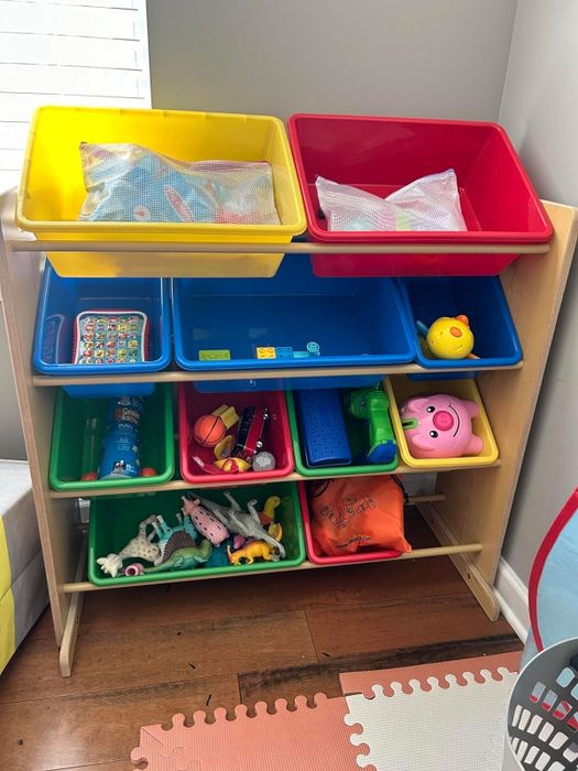 A toy organizer featuring multiple bins, each filled with toys and children's items, positioned within a play area.