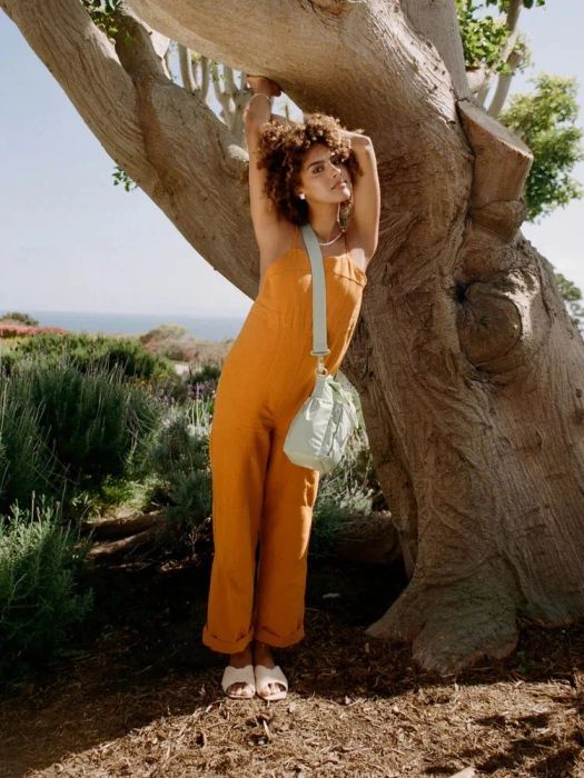 A model leans against a tree, wearing the Daisy-colored water bottle holder slung over their shoulder