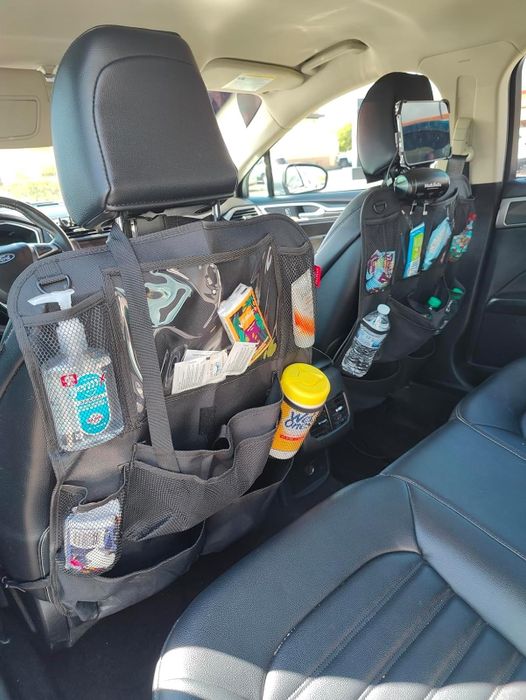 Backseat organizers filled with snacks, cleaning essentials, and a water bottle, mounted behind the driver and passenger seats in a car
