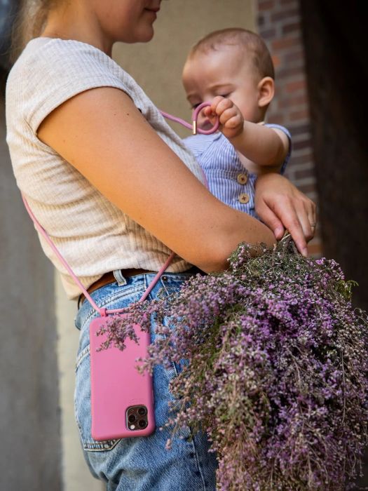 A model holds a baby while wearing a pink crossbody phone case across their body