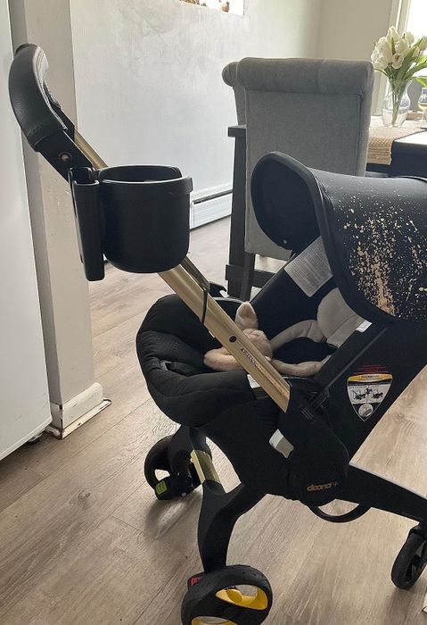 A baby stroller equipped with a cup holder and a speckled shade cover, with a child’s foot peeking out