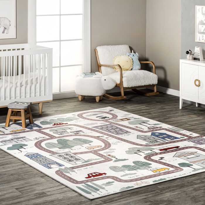 A children’s playroom featuring a themed rug, a crib, a rocking chair, and a side table filled with toys