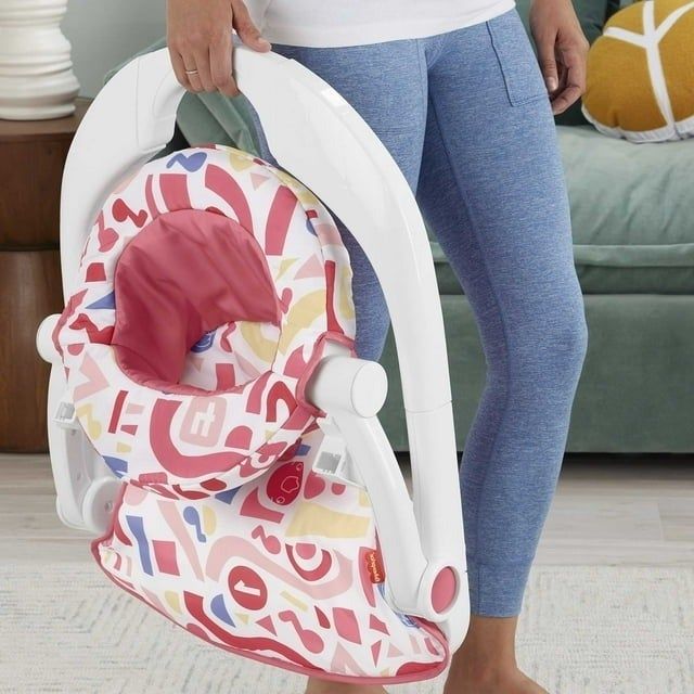 A person standing beside a folded, vibrantly patterned bouncer chair for babies
