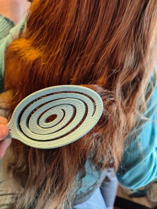 A person using a spiral detangler to gently work through long hair