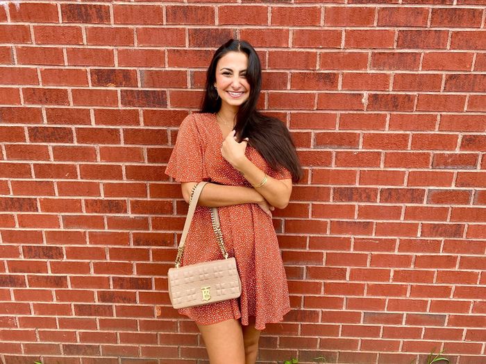 reviewer wearing the red dress in front of a brick wall, holding a pink purse