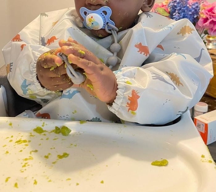 A reviewer-submitted photo of a baby with a pacifier, wearing a bib and sitting in a high chair, hands covered in food
