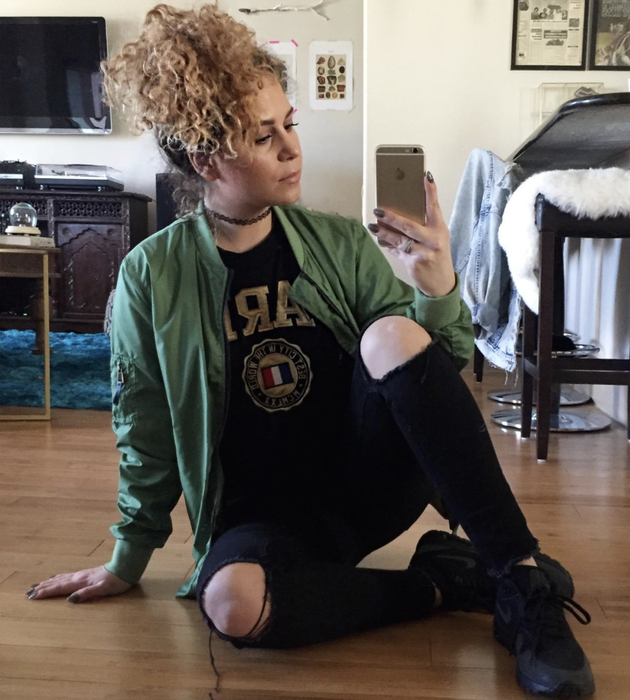 The reviewer is wearing a dark green bomber jacket paired with distressed black jeans.