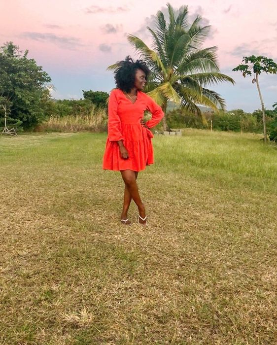 reviewer wearing the red dress in a grassy field with a palm tree in the background