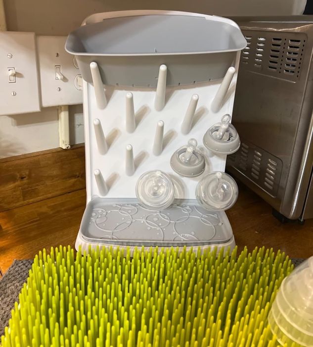 A bottle drying rack holding various baby bottle parts, positioned next to a green bottle brush