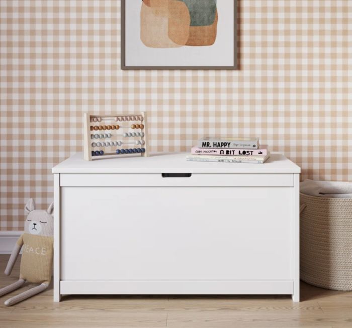 A white toy chest placed in a child’s room, topped with books and an abacus, surrounded by cute decorative items.