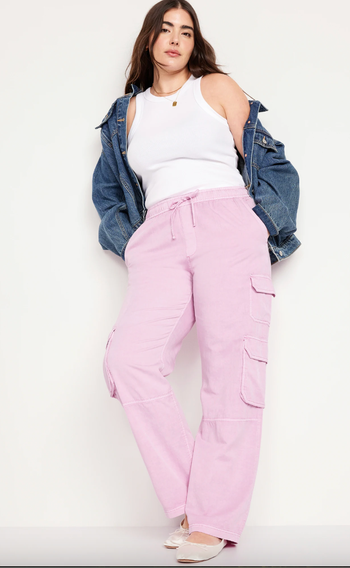 A model is shown wearing pink cargo pants, a white tank top, and an off-shoulder denim jacket.