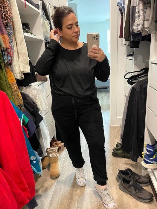 A person trying on a black outfit with sneakers, taking a selfie in a store mirror
