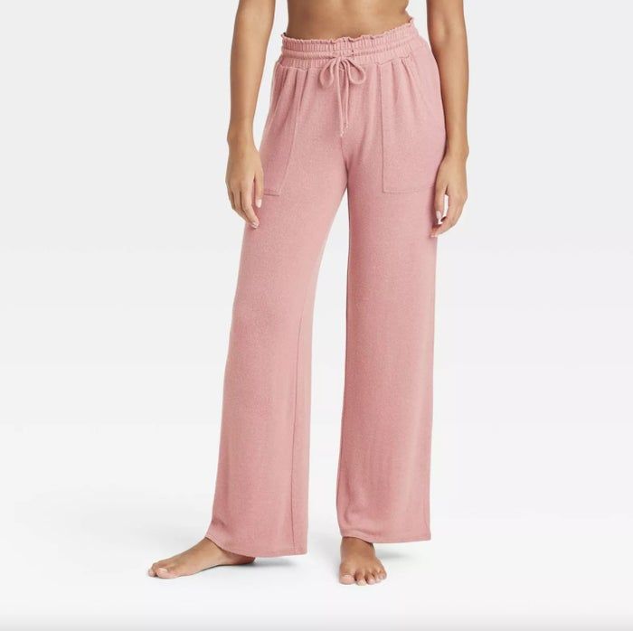 A person is shown barefoot, modeling loose-fitting, wide-leg pants featuring an elastic waistband and drawstring. The image captures only the lower body, from the waist down.