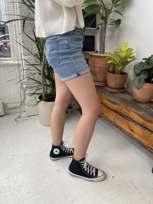 A writer wearing the shorts paired with hi-top black Converse, surrounded by plants in the background