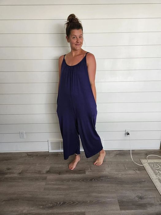 A woman in a casual sleeveless jumpsuit posing with a hand on her hip indoors
