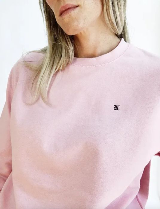 a model wearing a pink sweatshirt with a 'K' embroidered on it