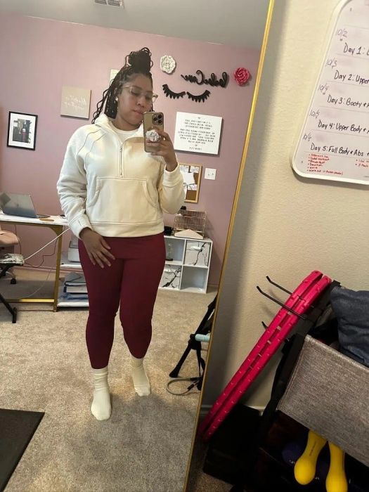 A person in a white hoodie and red leggings capturing a mirror selfie in a room filled with workout gear