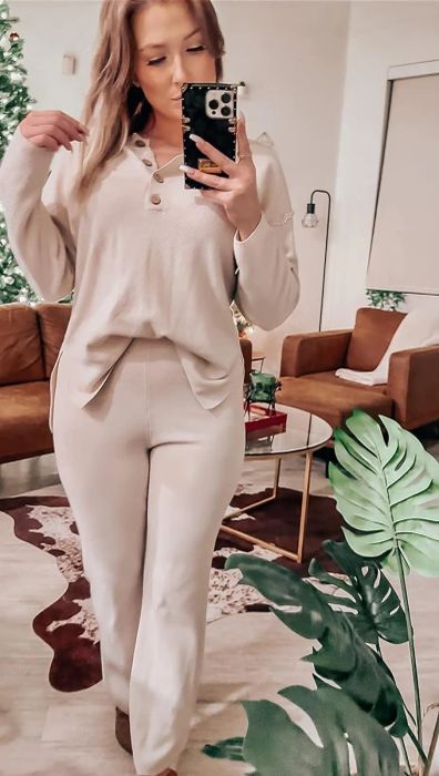 A person in a casual beige button-up shirt and matching pants taking a mirror selfie