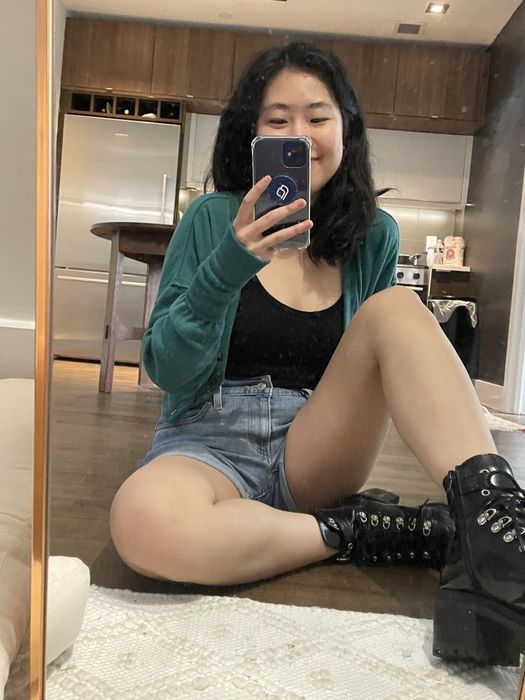 A writer taking a selfie, wearing shorts, combat boots, and a green cardigan.