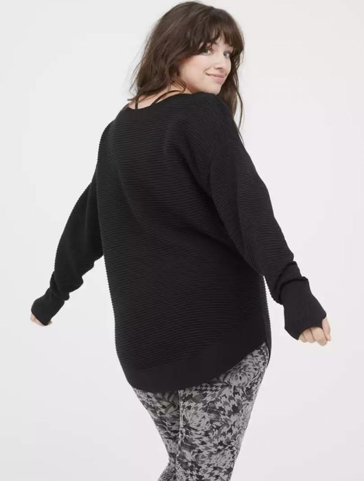 The model is looking over her shoulder while wearing the black sweater.
