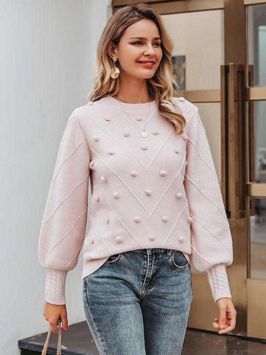 The model is wearing the sweater with lantern sleeves and playful pom-pom details.