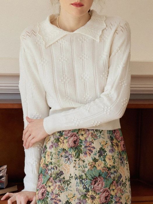 The model is styled in a white cable knit sweater with a collared design.