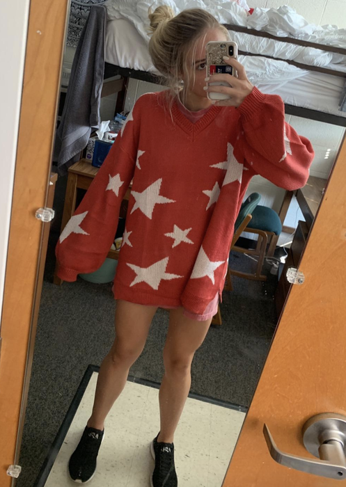The reviewer is wearing a red oversized sweater adorned with white stars.