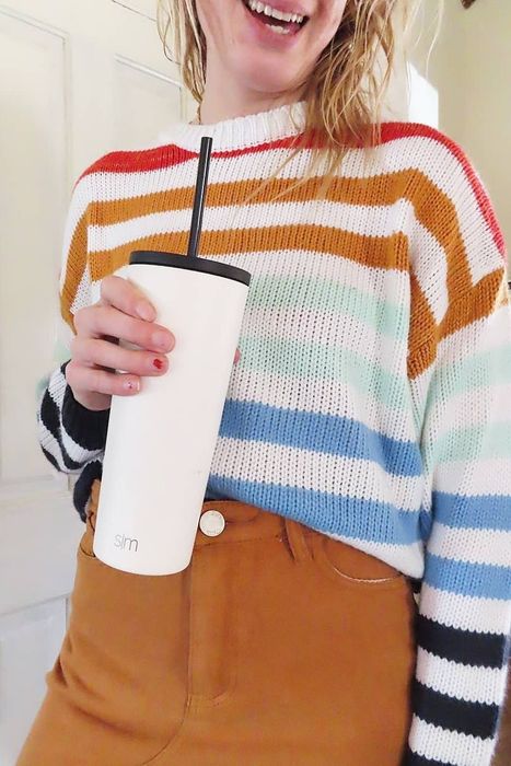 The reviewer is dressed in a vibrant rainbow-striped sweater paired with a chic brown skirt.