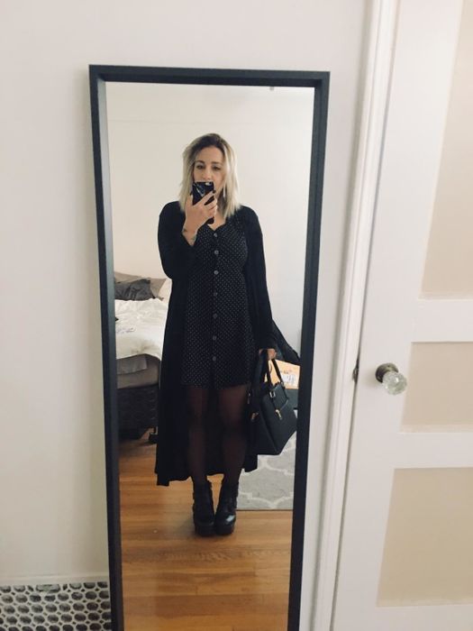 Reviewer wearing a long black cardigan over a black dress, black tights, and boots