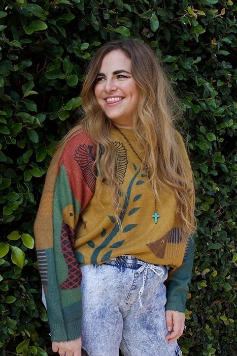 The reviewer is seen in a graphic sweater featuring a mix of green, red, and yellow hues.