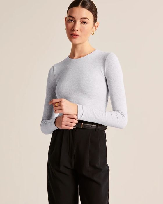 A model sporting a seamless long-sleeve tee in light gray, paired with black slacks for an effortlessly sleek look.