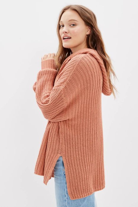 The model showcases a brown hoodie sweater, highlighting its longer back design from a side angle.