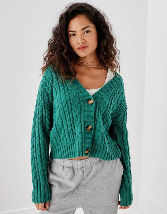 The model showcases a cropped green cable knit cardigan, effortlessly styled with casual sweatpants.