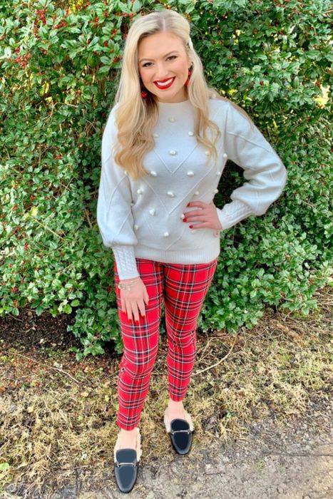The reviewer is styled in a gray pom-pom sweater paired with red plaid leggings.