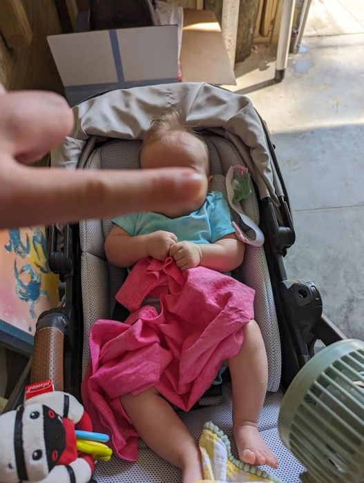 Reviewer's photo of a baby in a stroller holding a pink cooling towel. The baby's face is covered by the reviewer's finger