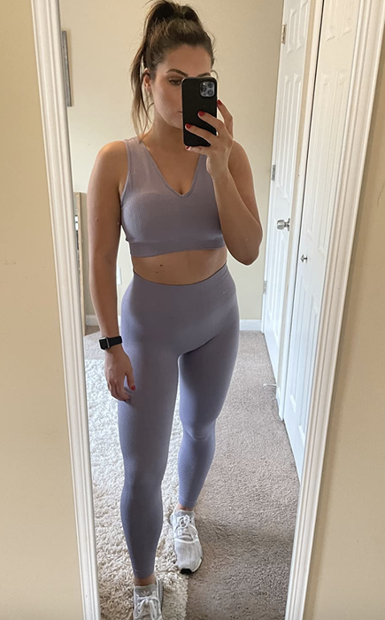 The reviewer is wearing a lilac sports bra and high-waisted leggings.