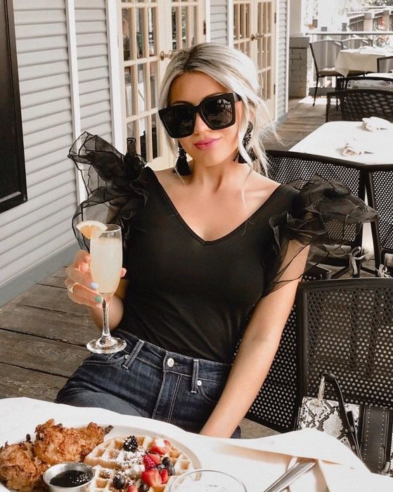 A reviewer showcasing the black sleeveless bodysuit featuring sheer tulle puff shoulders