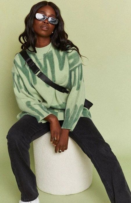 The model is wearing a mint green sweater adorned with abstract green designs.