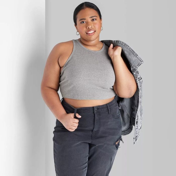 Model sporting a gray sleeveless crop top paired with high-waisted dark jeans, casually holding a denim jacket over her shoulder