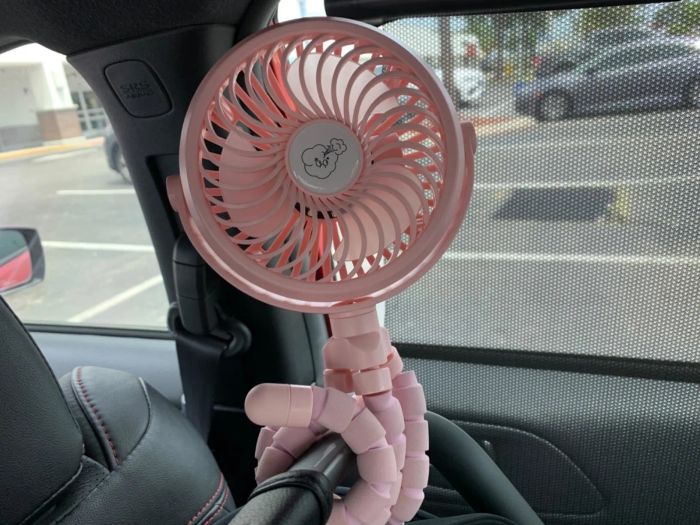 Reviewer's photo of a pink fan with bendable legs attached to a car seat inside a vehicle
