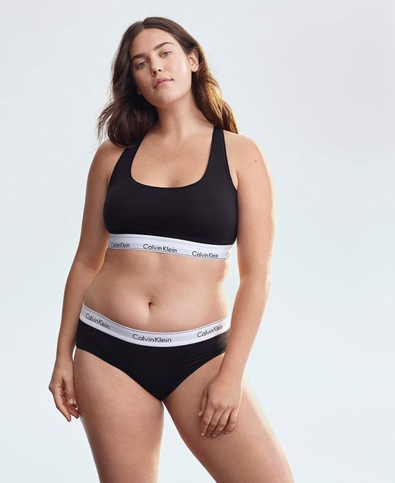A model wearing a black bralette featuring a white logo band, paired with matching underwear