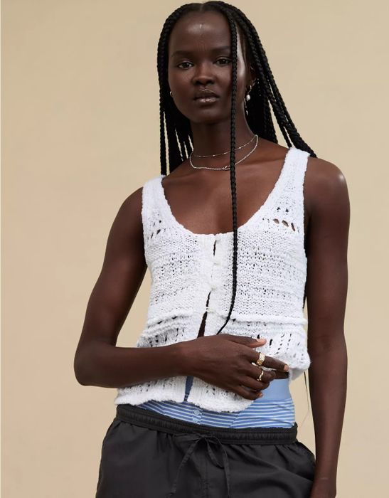 Model wearing a textured knit tank layered over a striped shirt and paired with dark pants, accessorized with rings and necklaces, featured in a fashion shopping article