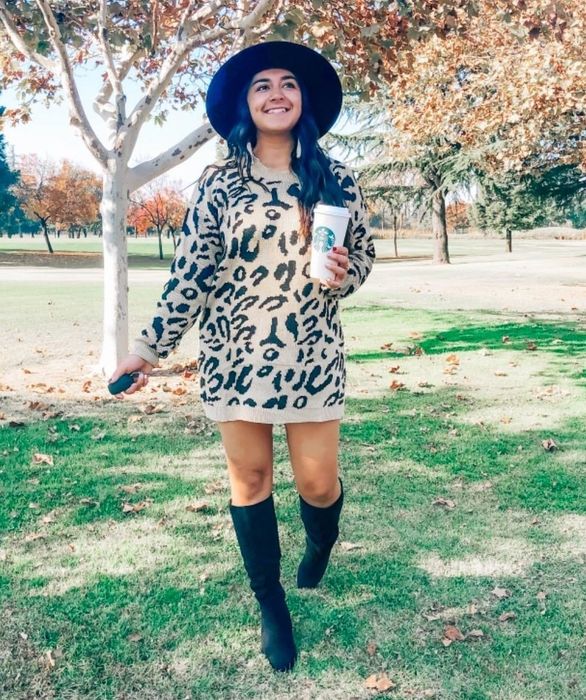 The reviewer styles a tan mid-thigh length leopard-print sweater as a dress, complemented by knee-high boots.