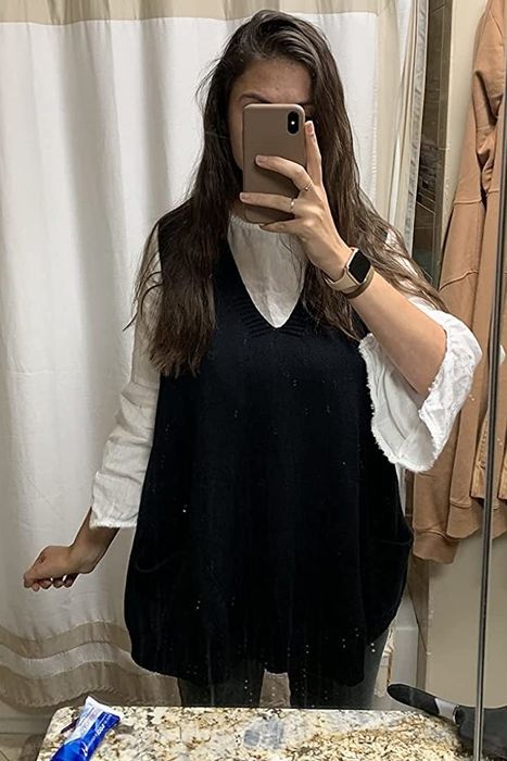 The reviewer pairs a long black sweater vest with a breezy white shirt for a polished yet relaxed ensemble.