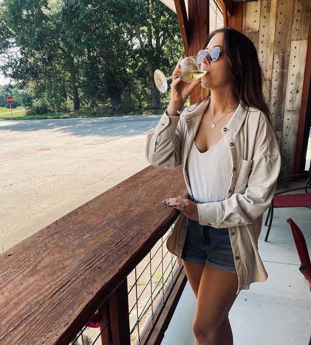 A reviewer wearing a beige oversized corduroy button-down over a beige top, paired with denim shorts, for a relaxed yet stylish vibe.