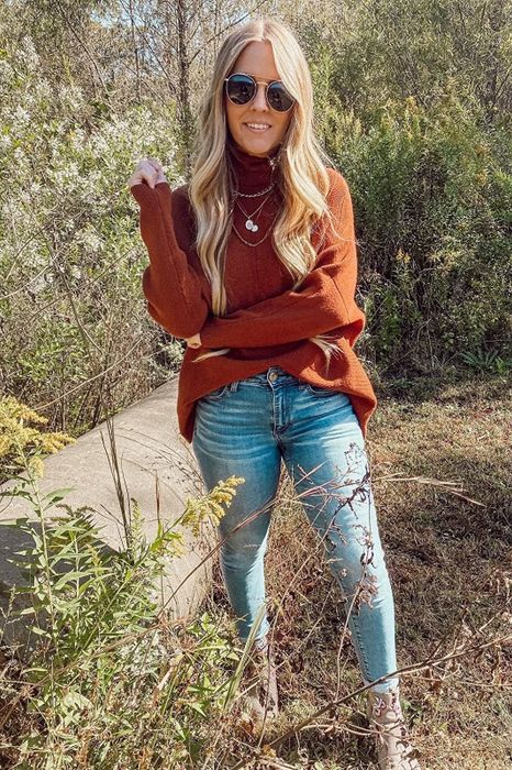 The reviewer is sporting a rust-colored sweater, tucked into jeans at the front for a polished look.