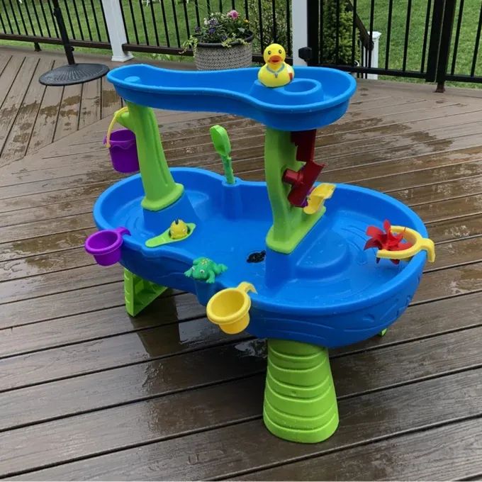 Reviewer's photo of the water play table featuring interactive toys like water wheels, buckets, and a rubber duck, placed on a wet wooden deck