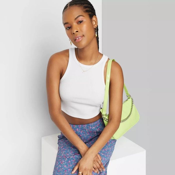Model confidently posing in a white crop tank top, a blue floral skirt, and a neon green shoulder bag for a fashion shopping feature