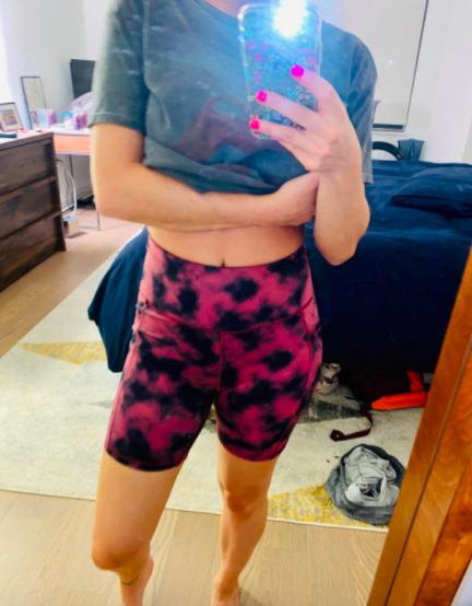 The reviewer is sporting high-rise bike shorts in a pink and black tie-dye pattern, paired with a casual T-shirt.