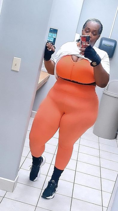 Individual snapping a mirror selfie in vibrant orange activewear while holding a phone